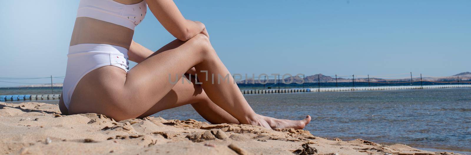 Fit sexy attractive woman sitting on the beach sunbathing by Desperada