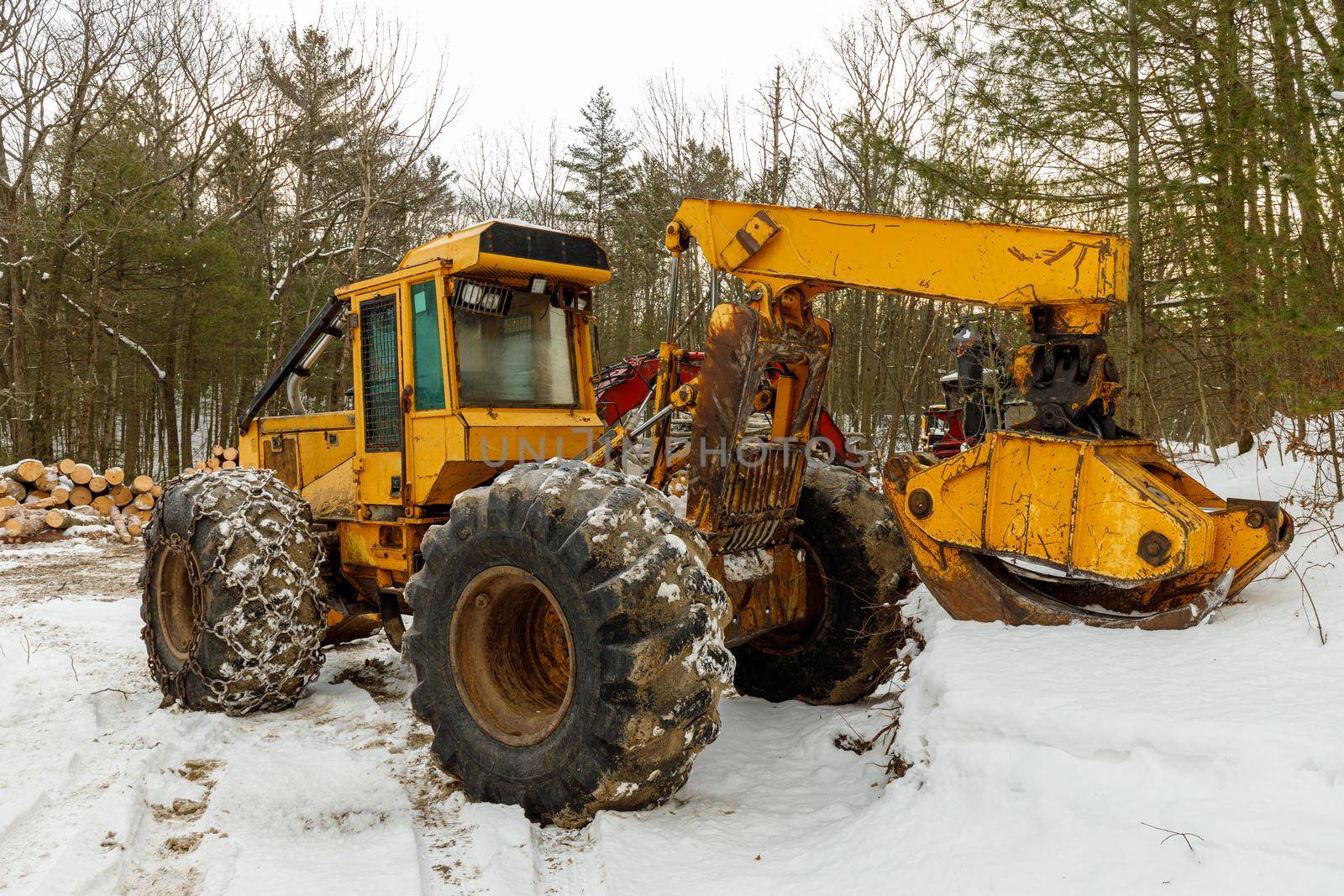 A Yellow Log Skidder Parked in the Snow. A pile of logs is in the background if this logging site. High quality photo