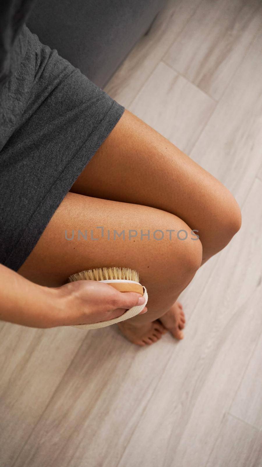 Woman holding wooden brush and doing dry massage on her legs. Self care concept by natali_brill