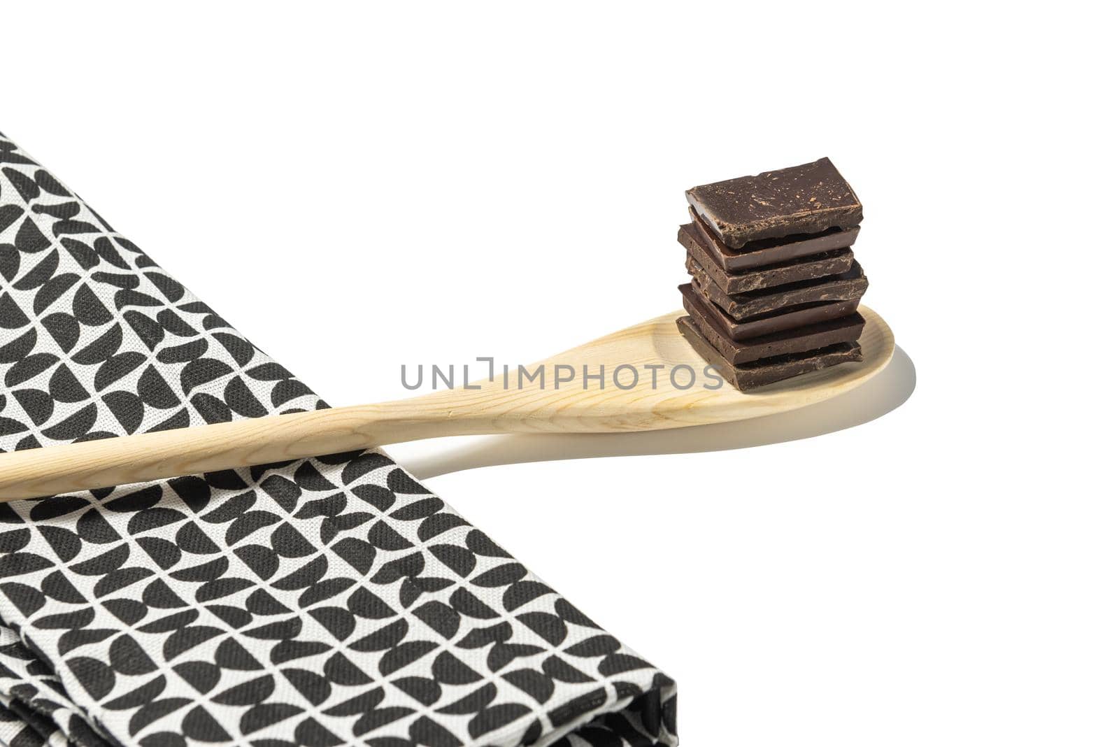 close up of chocolate pieces on wooden spoon with a kitchen napkin on a white background.