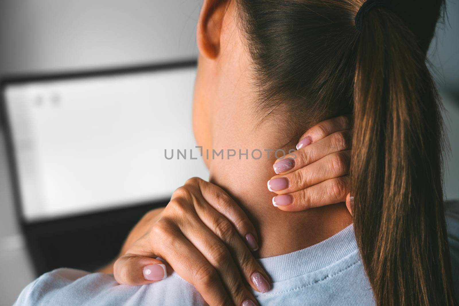 Young woman suffering from neck pain after working on pc and massaging neck to relieve pain. High quality photo