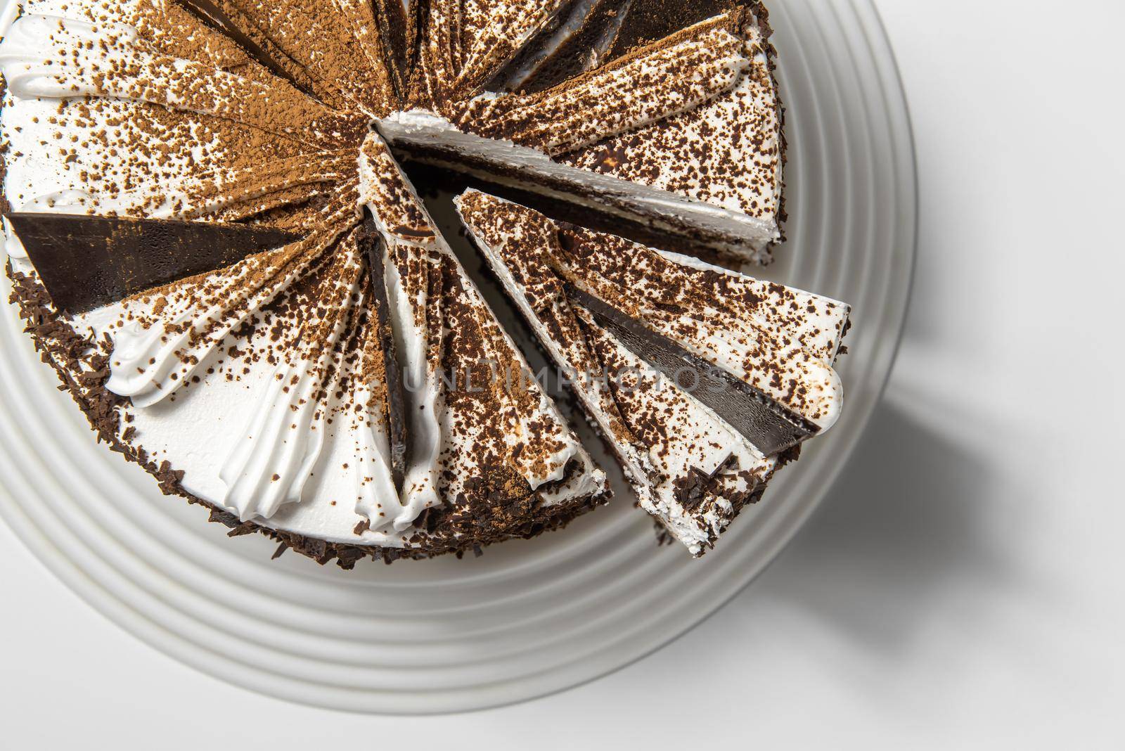 cake with chocolate, sprinkled with chocolate chips, on a tray on a white background with a cut piece. top view.