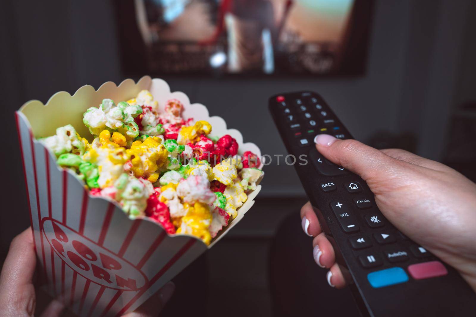Woman watching TV or watching movie with remote control and popcorn at home. First person view. High quality photo