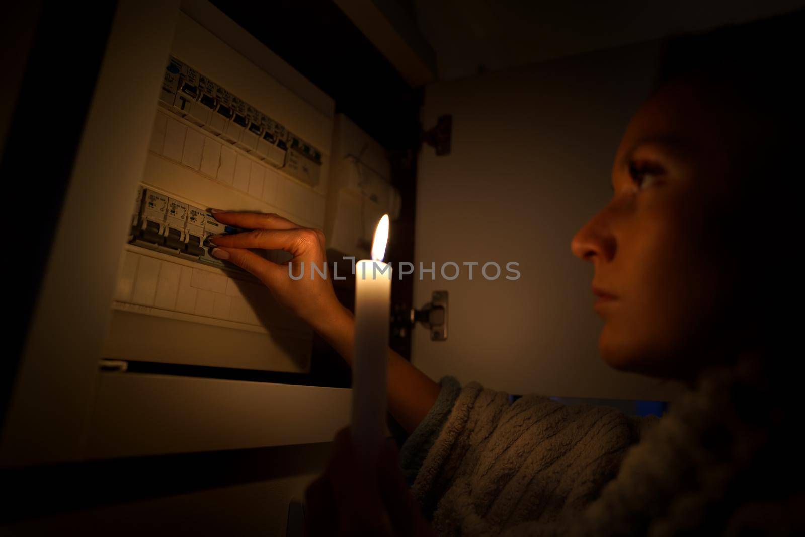 Woman in total darkness investigating fuse box at home during power outage or blackout. No electricity concept. High quality photo