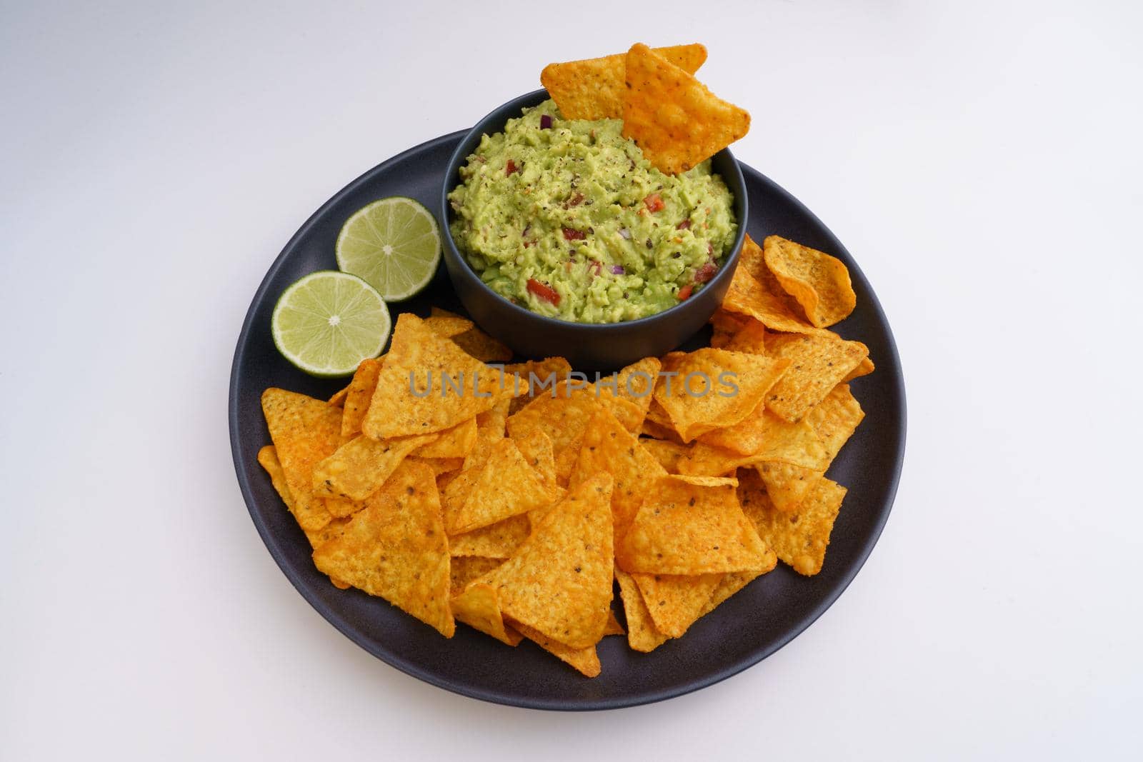Guacamole sauce and tortilla chips or nachos in black plate isolated on a white background by DariaKulkova