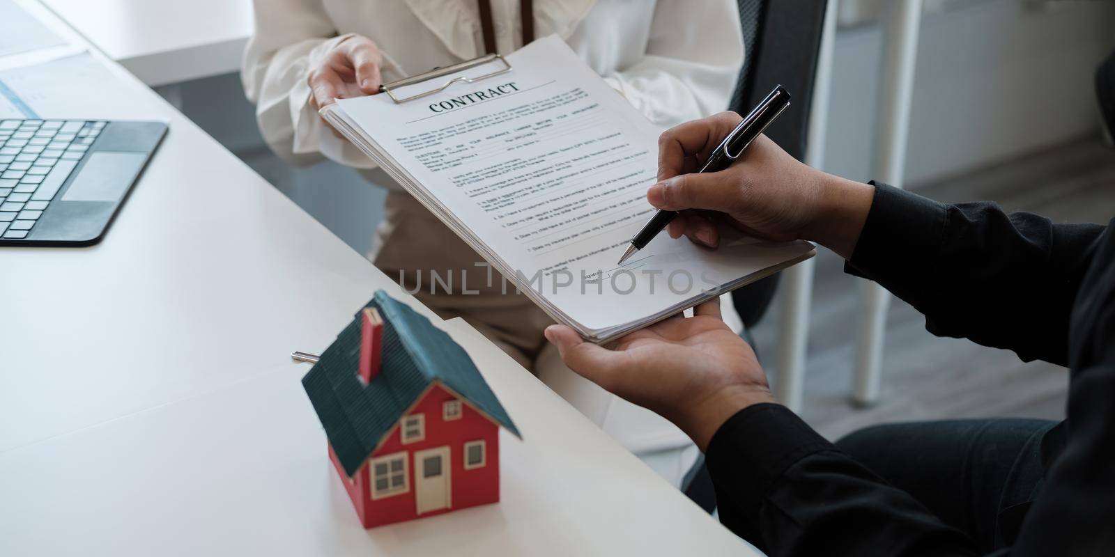 Real estate brokers point to a contract paper and advise customers to sign their names. customer sign agreement contract signature for buy or sell house. Real estate concept contact agreement concept.