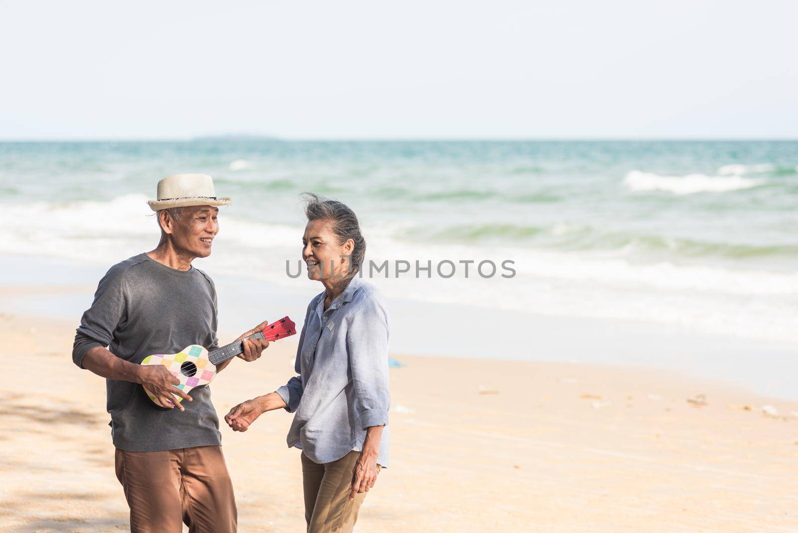 Happy senior couple relaxing outdoors singing and playing acoustic guitar at beach near sea sunny day by Sorapop