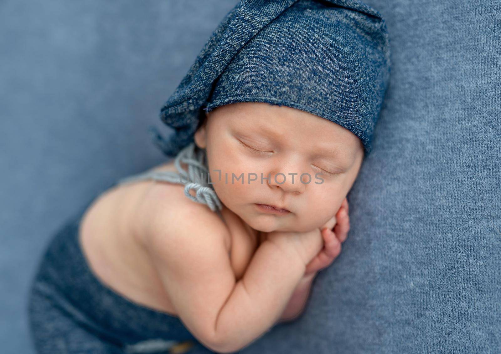 Newborn baby boy wearing knitted hat sleeping and holding hands under his cheeks. Infant kid napping