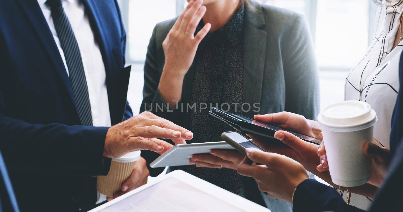 Technology helps our business move faster. Cropped shot of an unrecognizable group of businesspeople standing and using technology while in the office. by YuriArcurs