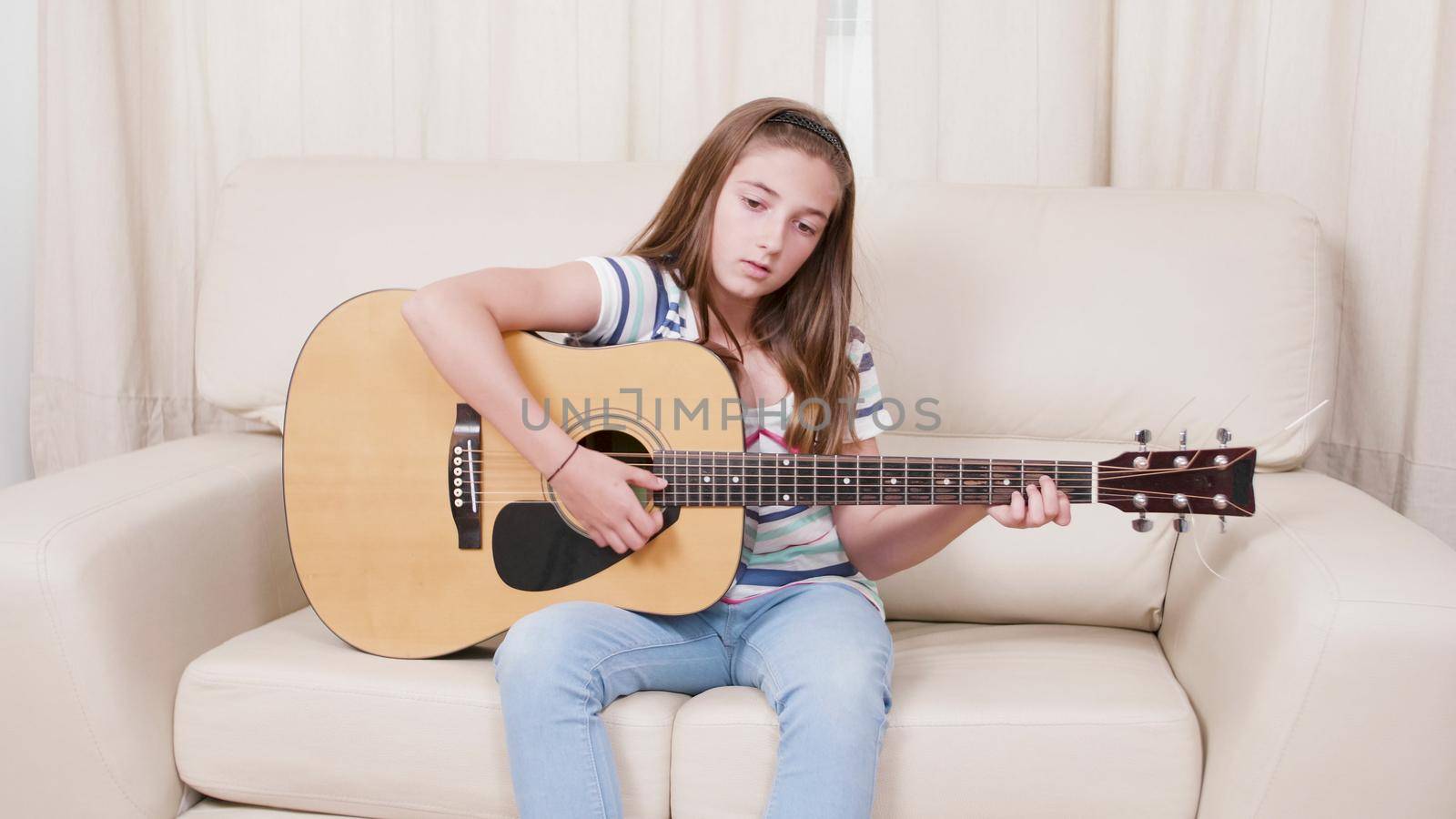 Young guitarist child sitting on sofa holding guitar learning how to sing by DCStudio