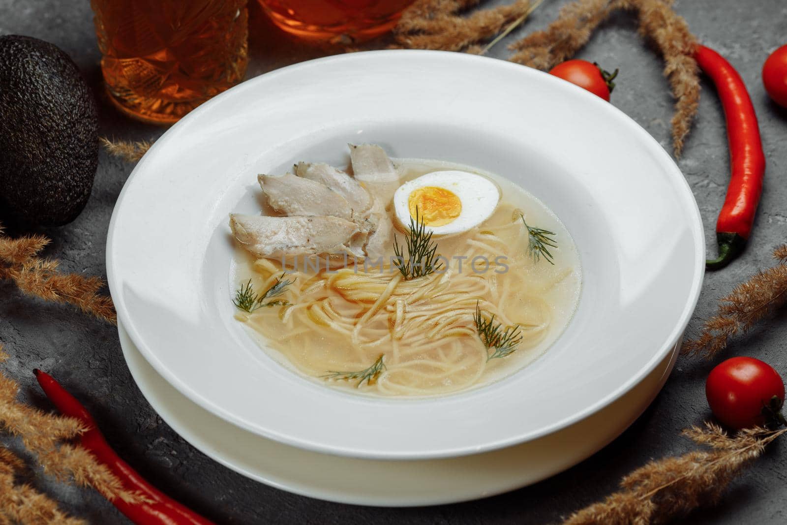 Chicken soup with noodles and vegetables in white bowl.