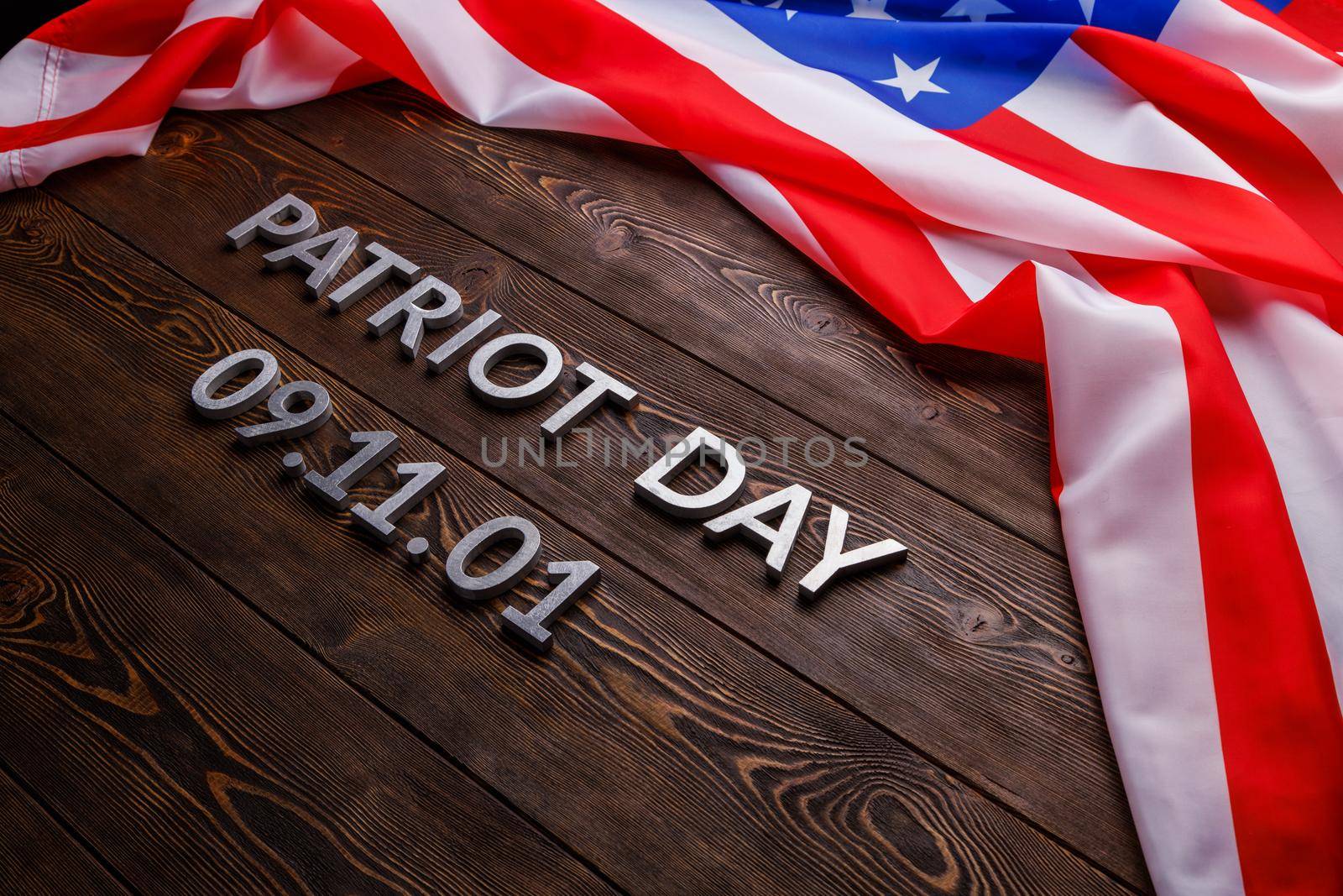 the words patriot day laid with silver metal letters on wooden board surface with crumpled usa flag above