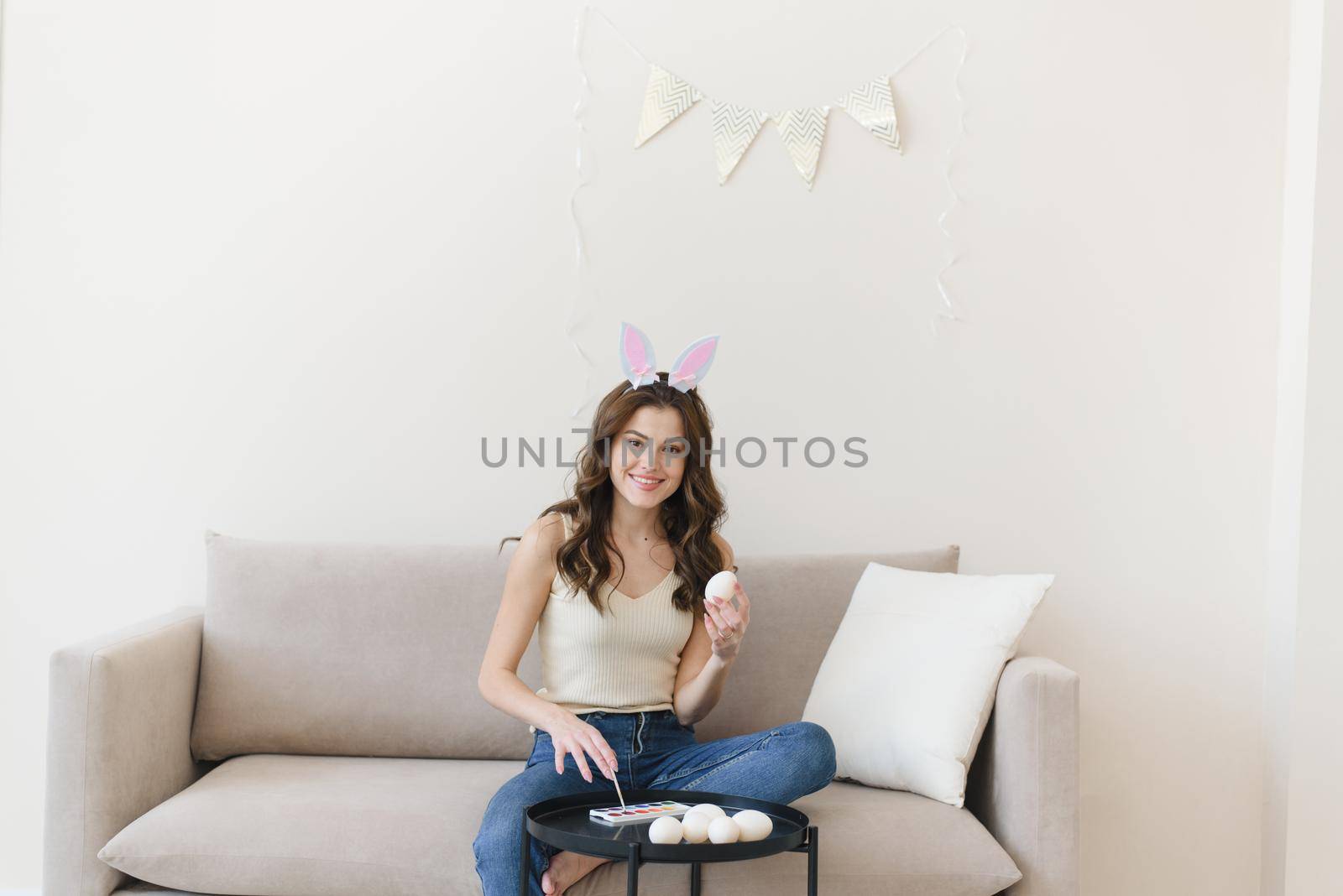 Pretty woman painting Easter egg at home looking at camera. Easter preparation