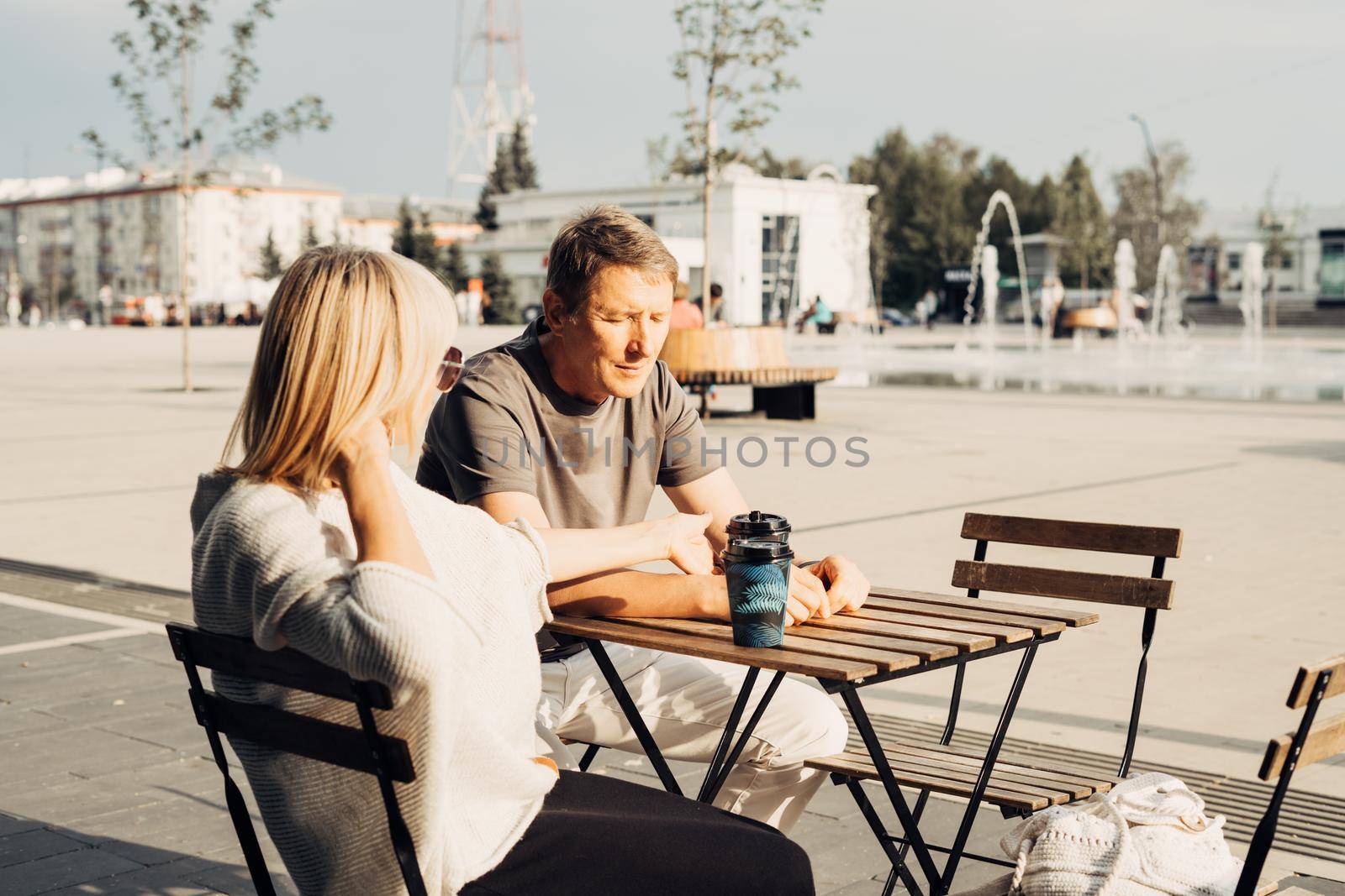 An adult mature happy couple in love in a street cafe order coffee. A blonde caucasian man and woman spend time together. Senior wife and husband walking outdoors