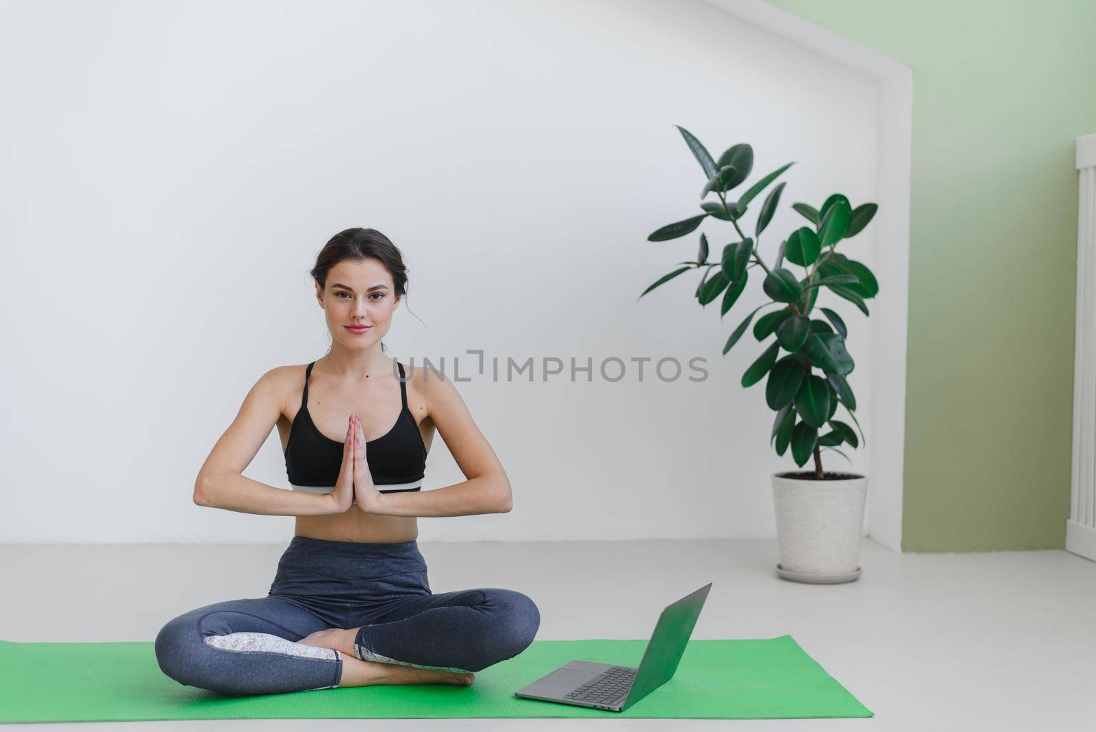 Young woman doing sports and yoga at home using a laptop. Advertisement for yoga courses