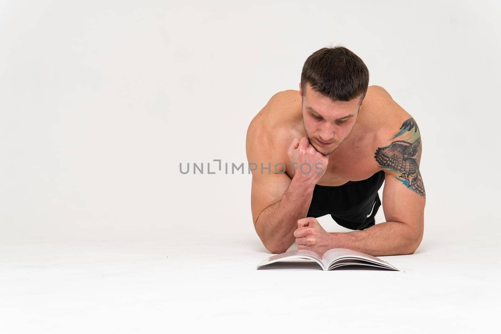Bodybuilder reads the book on a white background isolated at the bottom of his head on his hands bodybuilder reading, muscle glasses chest muscles, sexy fit. Health winner gym, vision tan by 89167702191