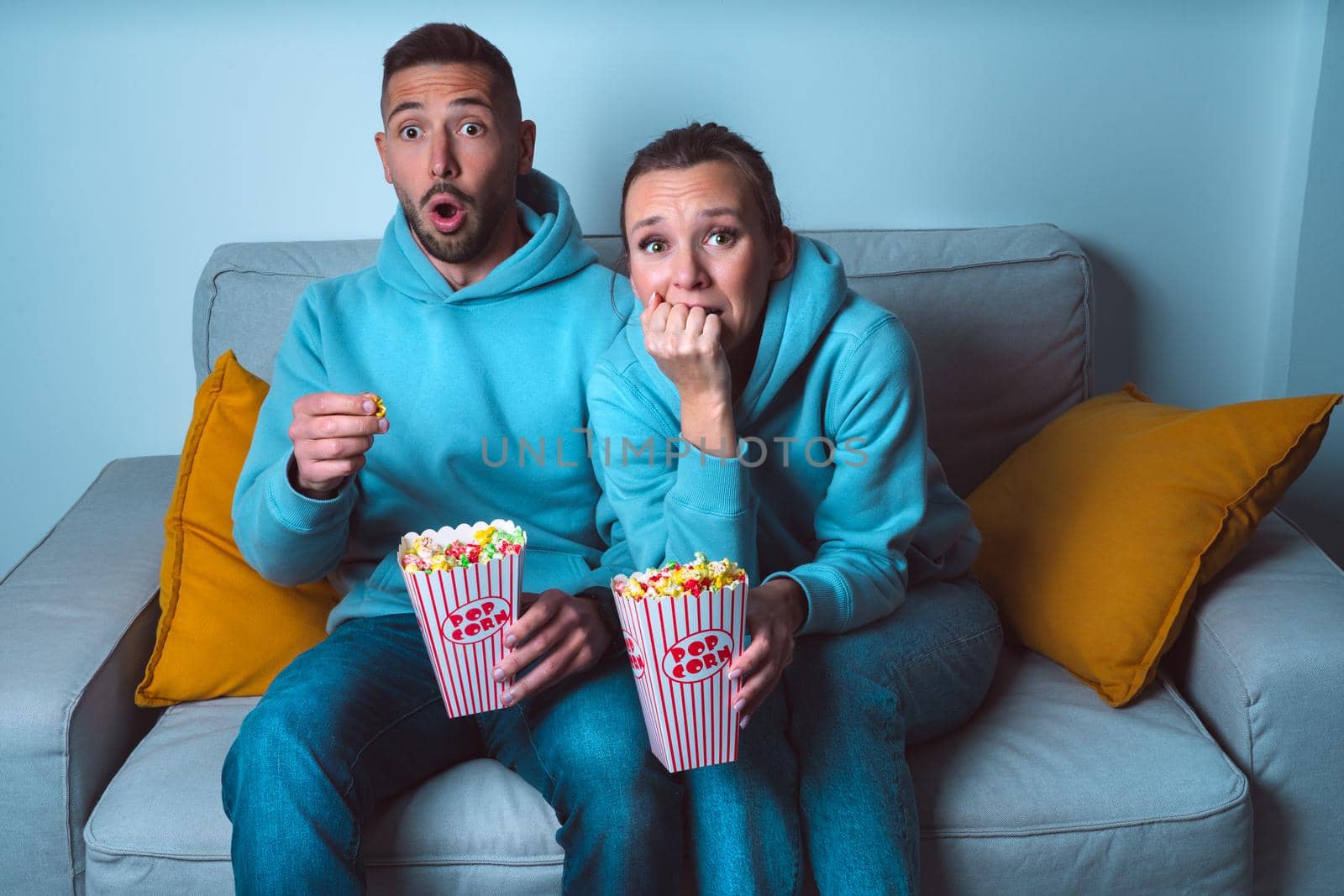 Young couple with popcorn watching horror or scary movie at home by DariaKulkova