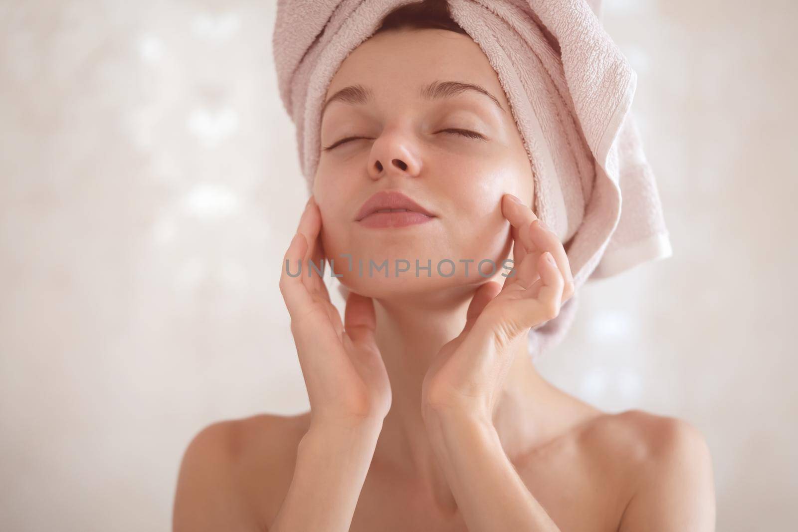 A young girl touches her delicate, clean, moisturized face skin with her hands, a woman takes care of the health and beauty of her body in the bathroom.