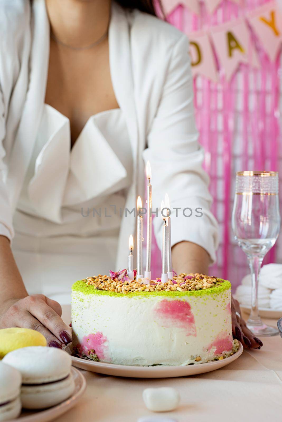 Birthday party. Birthday tables. Attractive woman in white party clothes preparing birthday table with cakes, cakepops, macarons and other sweets, making wish