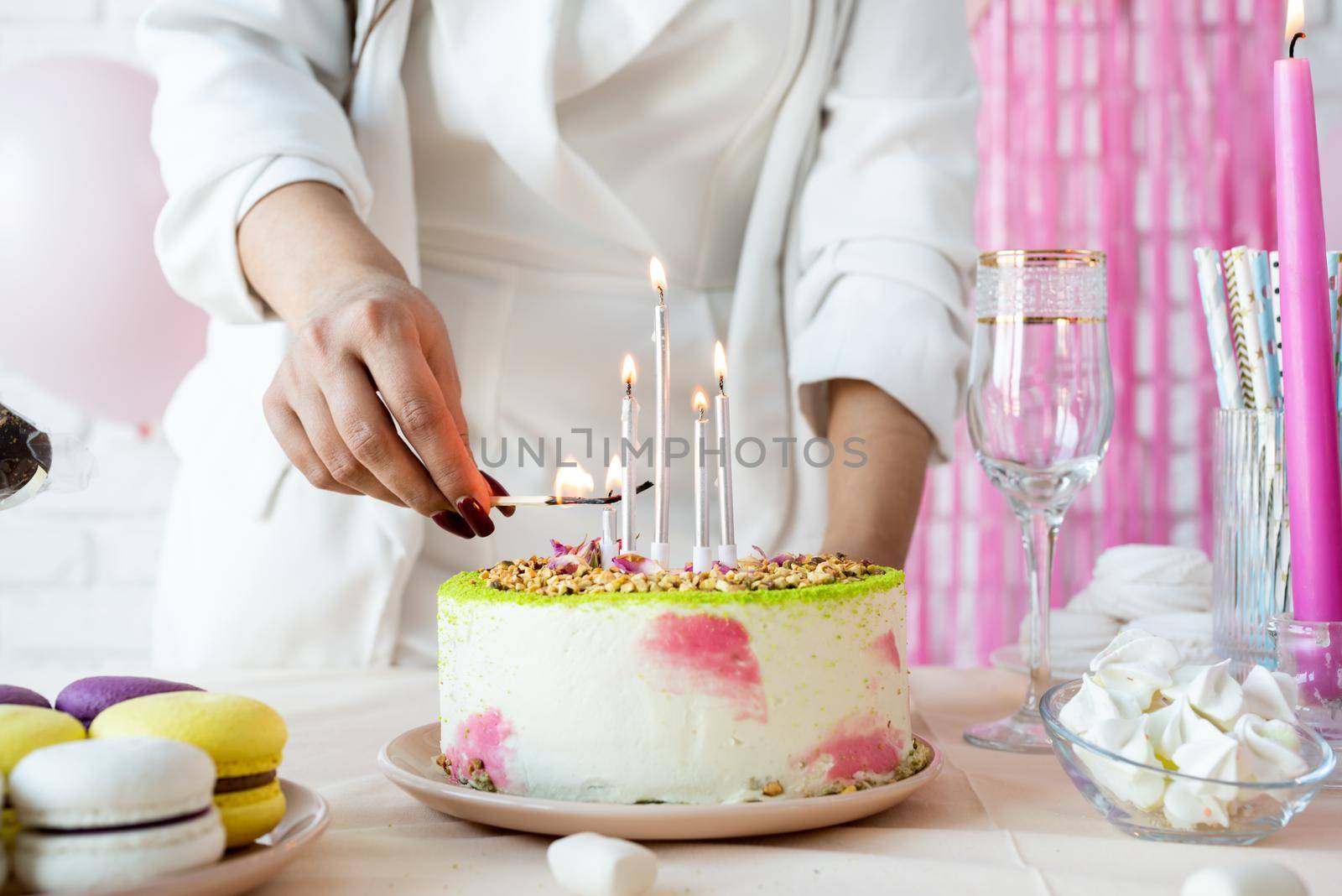 Woman in white party clothes preparing birthday table, lighting the candles by Desperada