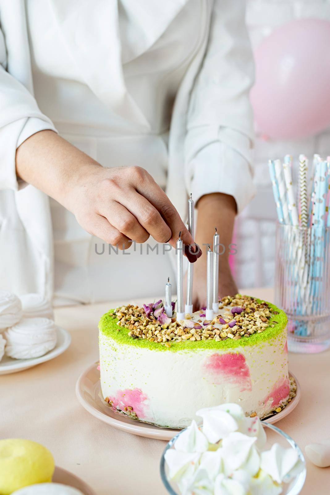 Birthday party. Attractive woman in white party clothes preparing birthday table, putting candles to cake