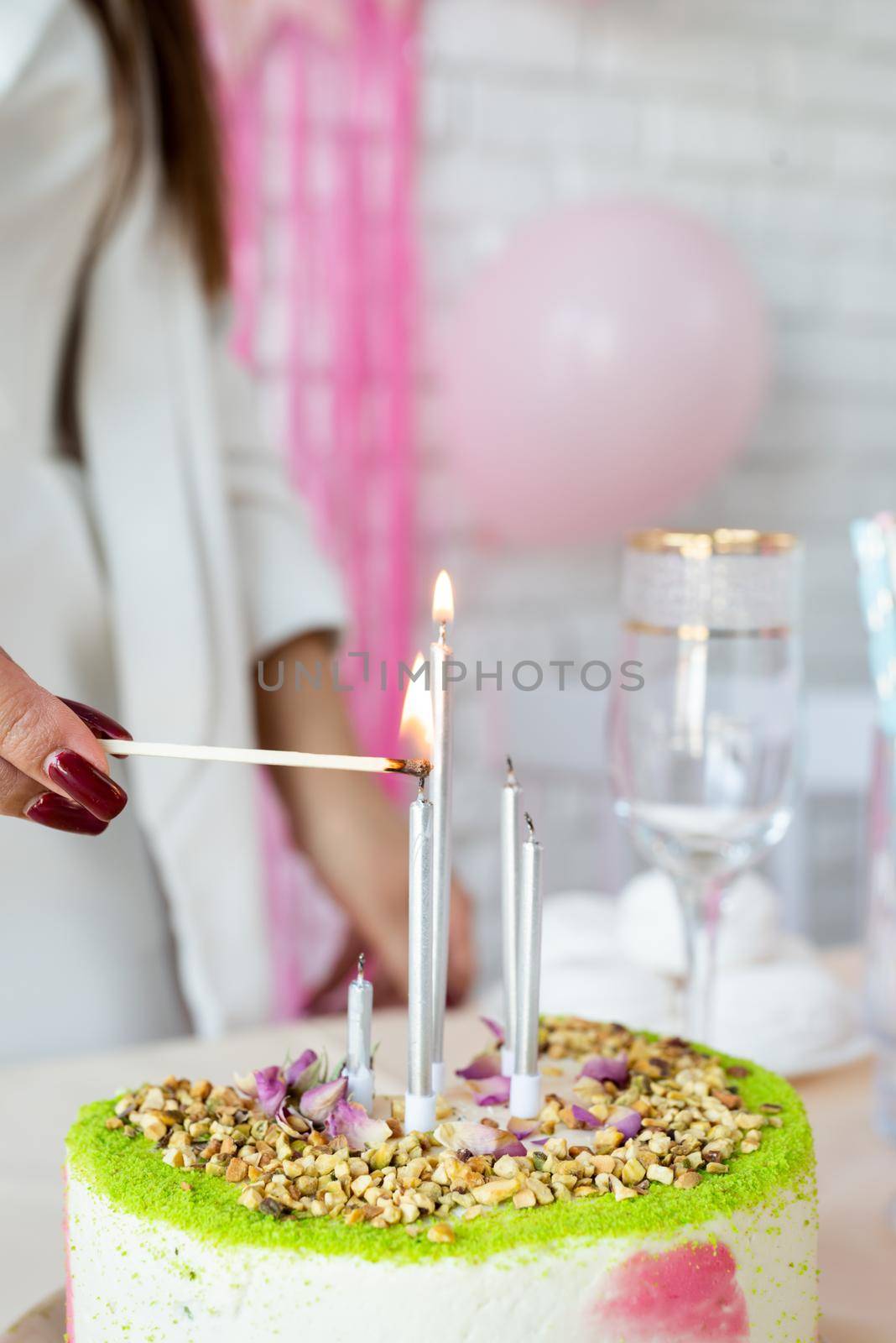 Birthday party. Birthday tables. Attractive woman in white party clothes preparing birthday table with cakes, cakepops, macarons and other sweets, lighting the candles