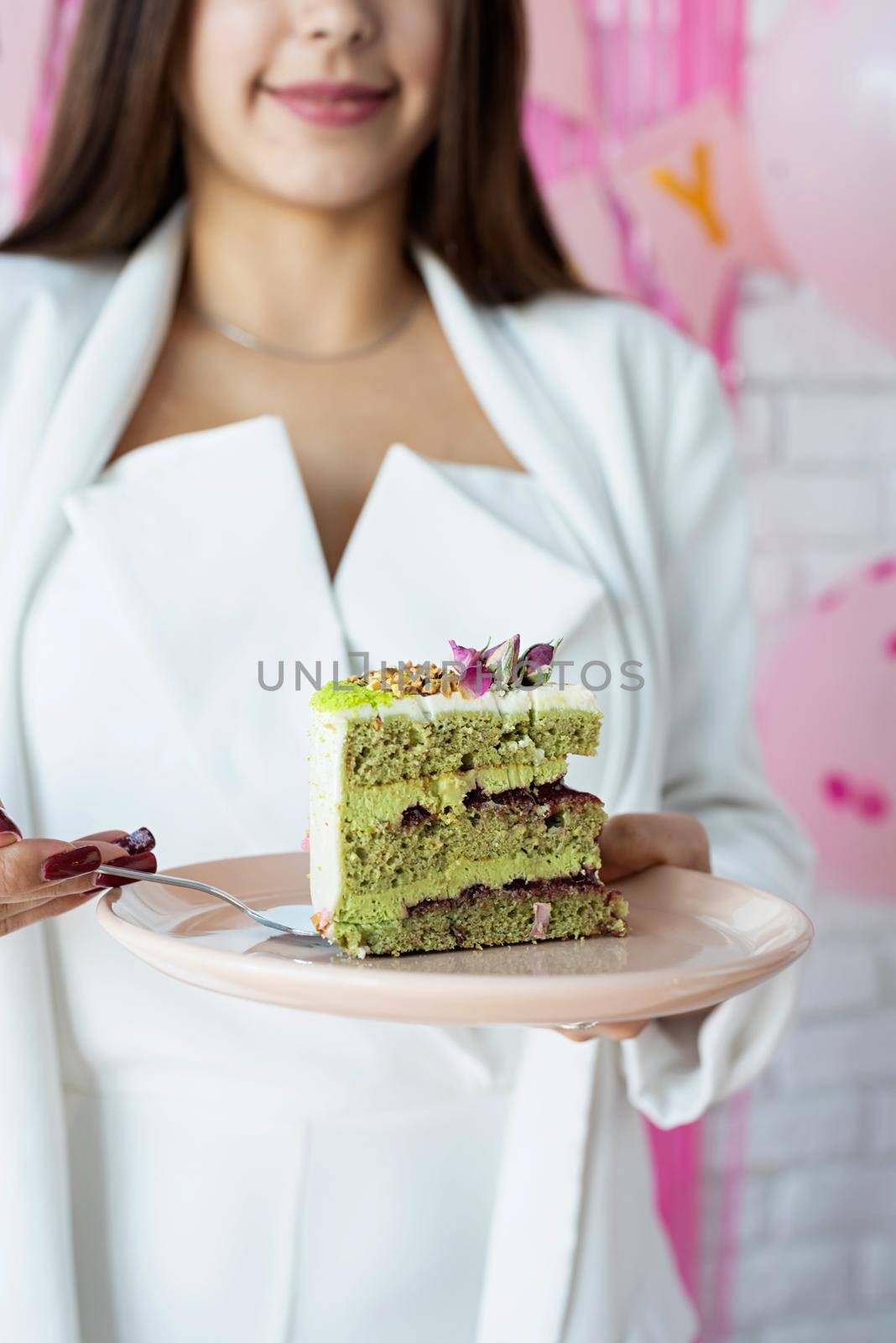Birthday party. Birthday tables. Attractive woman in white party clothes preparing birthday table, celebrating and holding a piece of pistachio cake