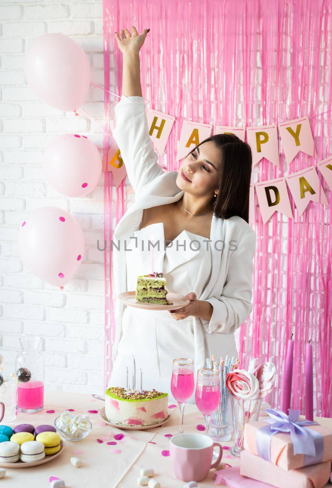 Birthday party. Birthday tables. Attractive woman in white party clothes preparing birthday table, celebrating and holding a piece of pistachio cake
