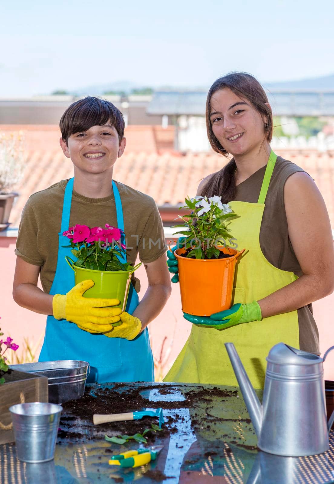 Two teenage holding plant pots while smiling on the terrace