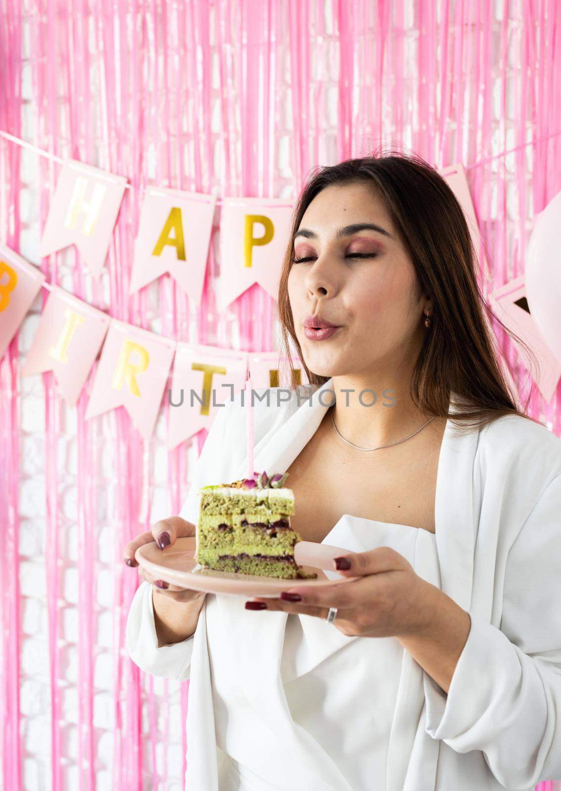 Birthday party. Birthday tables. Attractive woman in white party clothes celebrating birthday and holding a piece of pistachio cake