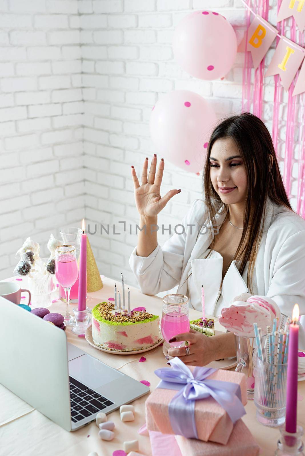 Birthday party. Birthday tables. Attractive brunette woman in white party clothes celebrating birthday using video call chatting with friends