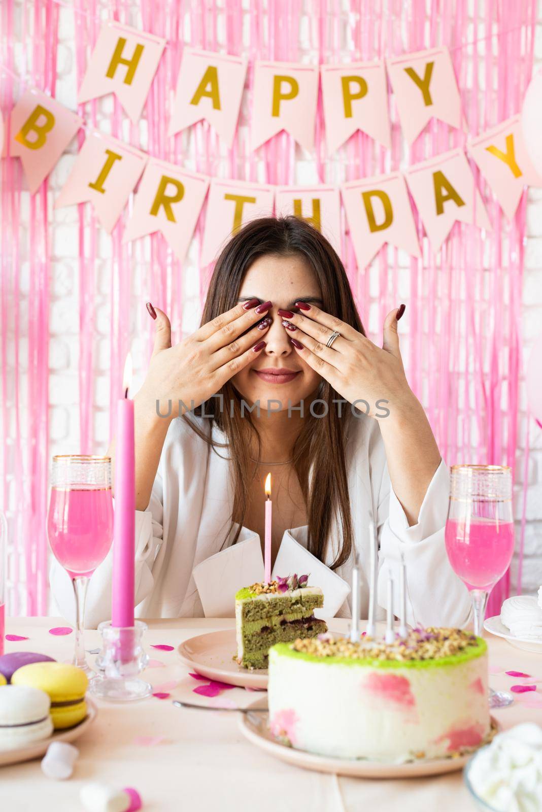 Birthday party. Birthday tables. Attractive brunette woman in white party clothes preparing birthday table with cakes, cakepops, macarons and other sweets, making wish