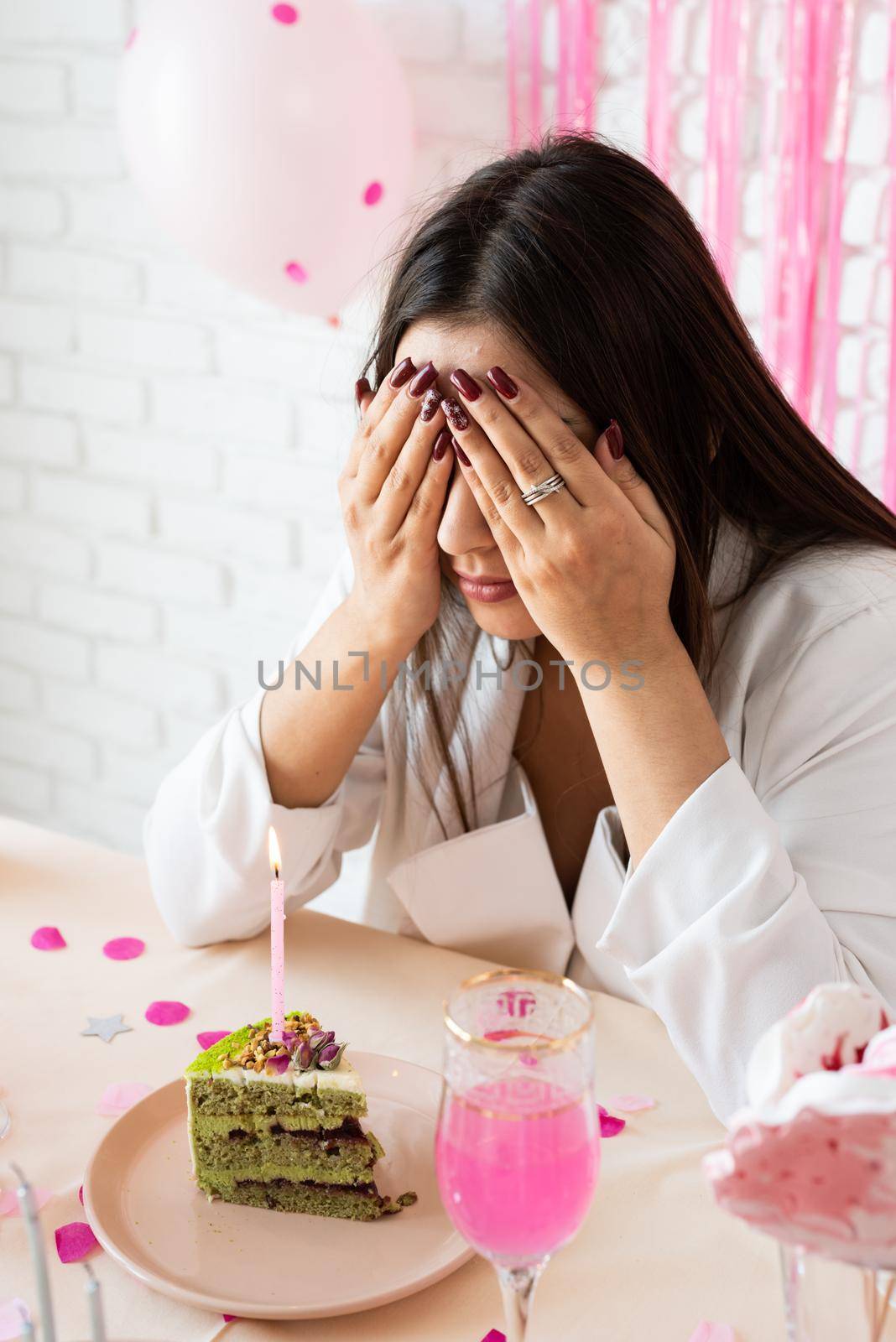 Birthday party. Birthday tables. Attractive brunette woman in white party clothes preparing birthday table with cakes, cakepops, macarons and other sweets, making wish