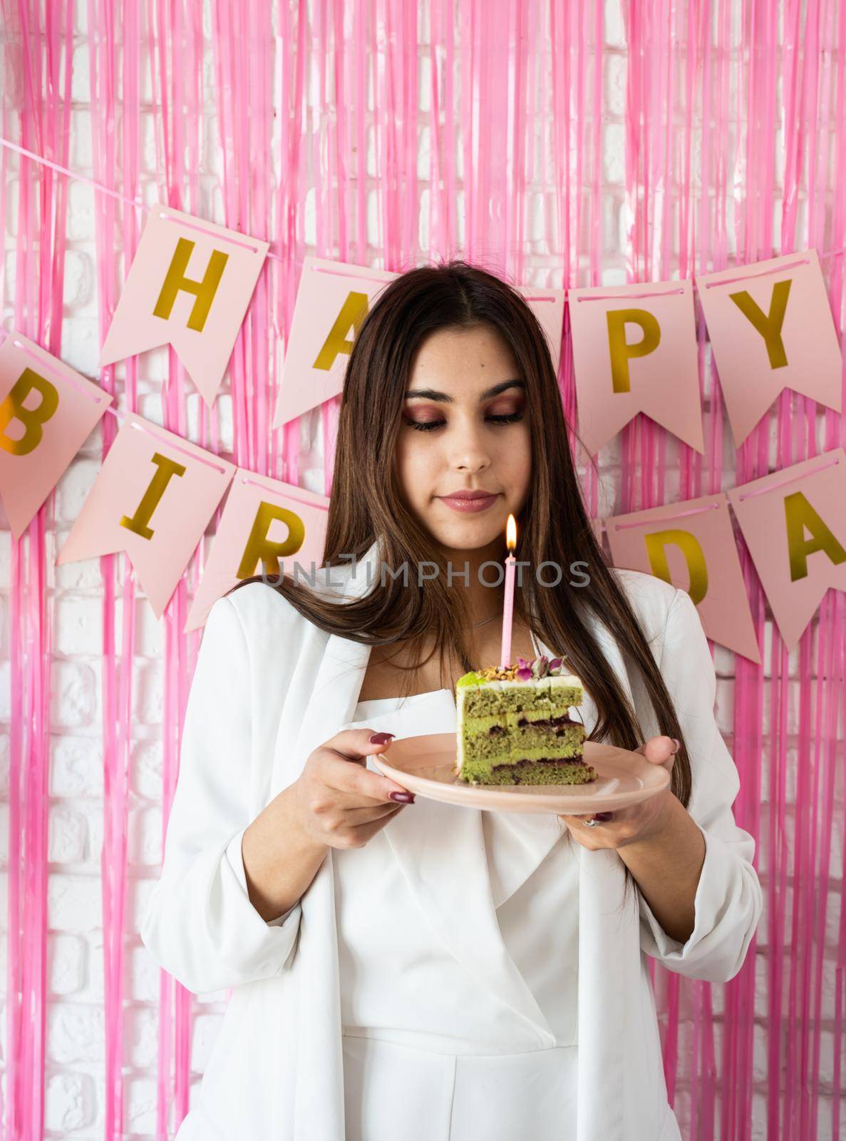Birthday party. Birthday tables. Attractive brunette woman in white party clothes preparing birthday table with cakes, cakepops, macarons and other sweets, making wish