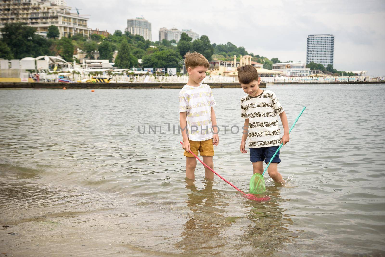 Two sibling little brother boy exploring the beach at low tide walking towards the sea coast. Friendship happy childhood concept by Kobysh