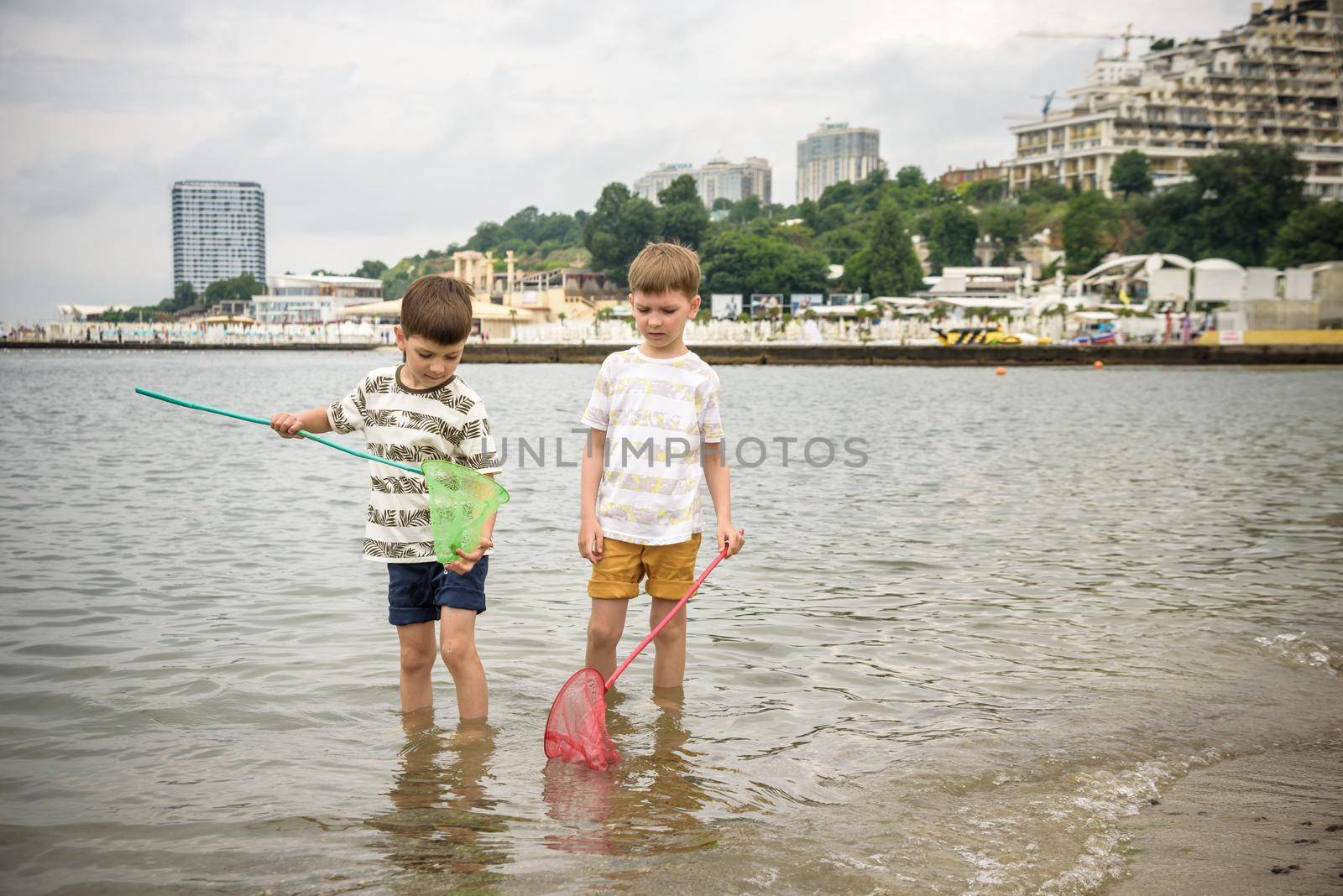 Two sibling little brother boy exploring the beach at low tide walking towards the sea coast. Friendship happy childhood concept.