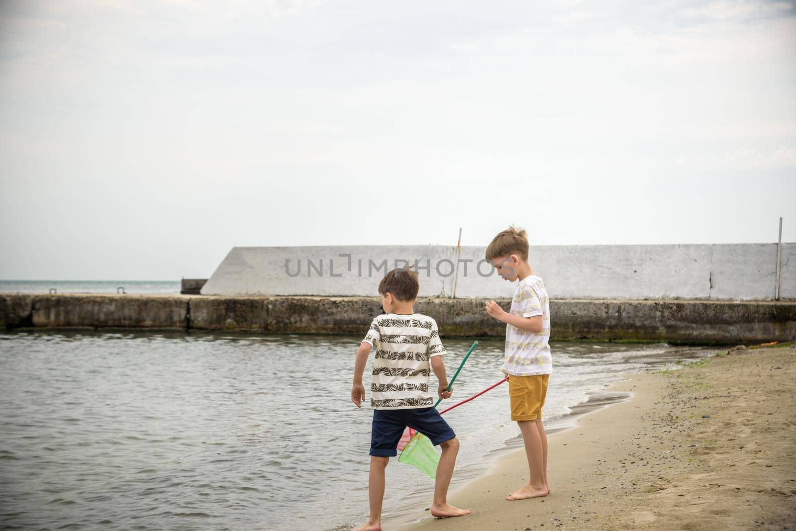 Two sibling little brother boy exploring the beach at low tide walking towards the sea coast. Friendship happy childhood concept by Kobysh