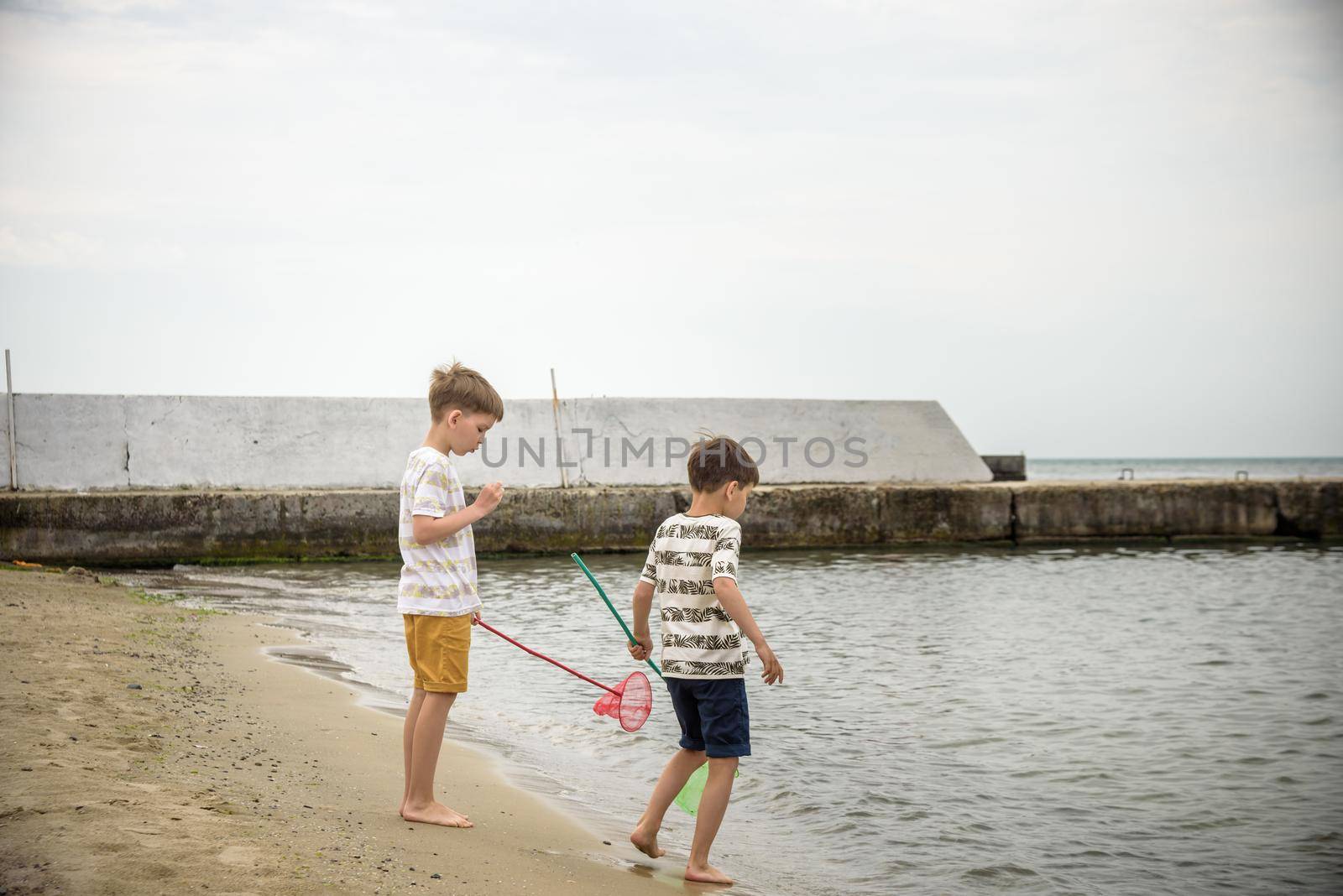 Two sibling little brother boy exploring the beach at low tide walking towards the sea coast. Friendship happy childhood concept.