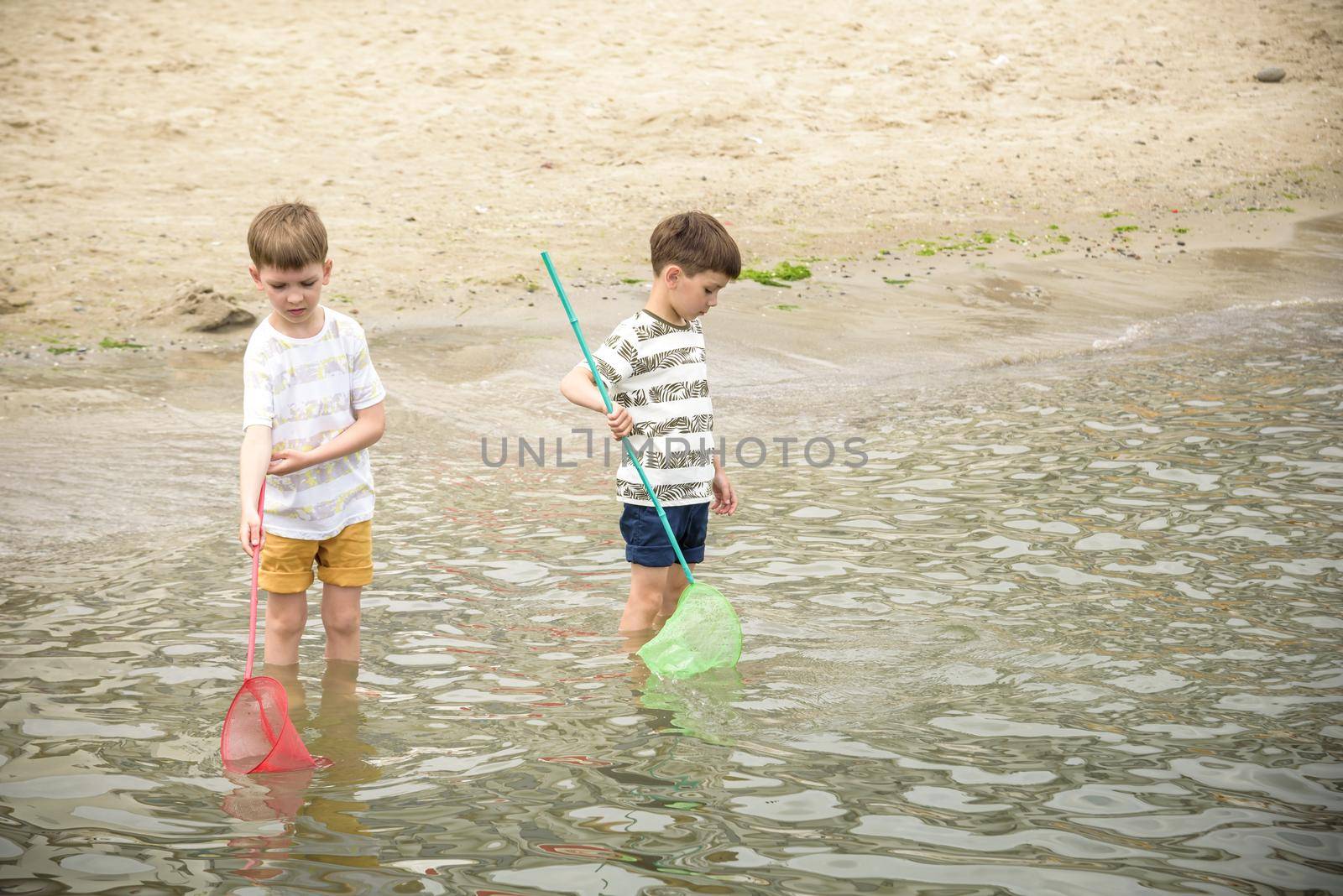 Two sibling little brother boy exploring the beach at low tide walking towards the sea coast. Friendship happy childhood concept.