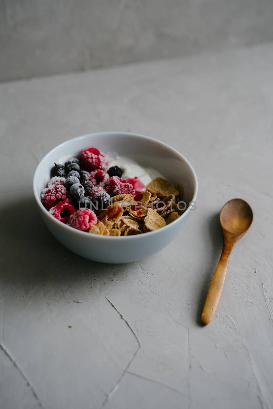 Healthy breakfast with berries, cereals and natural yogurt. Multi-lacquered cereals for breakfast. Berries in ice. Frozen raspberries and black currants. Delicious and healthy breakfast. Wooden spoon.