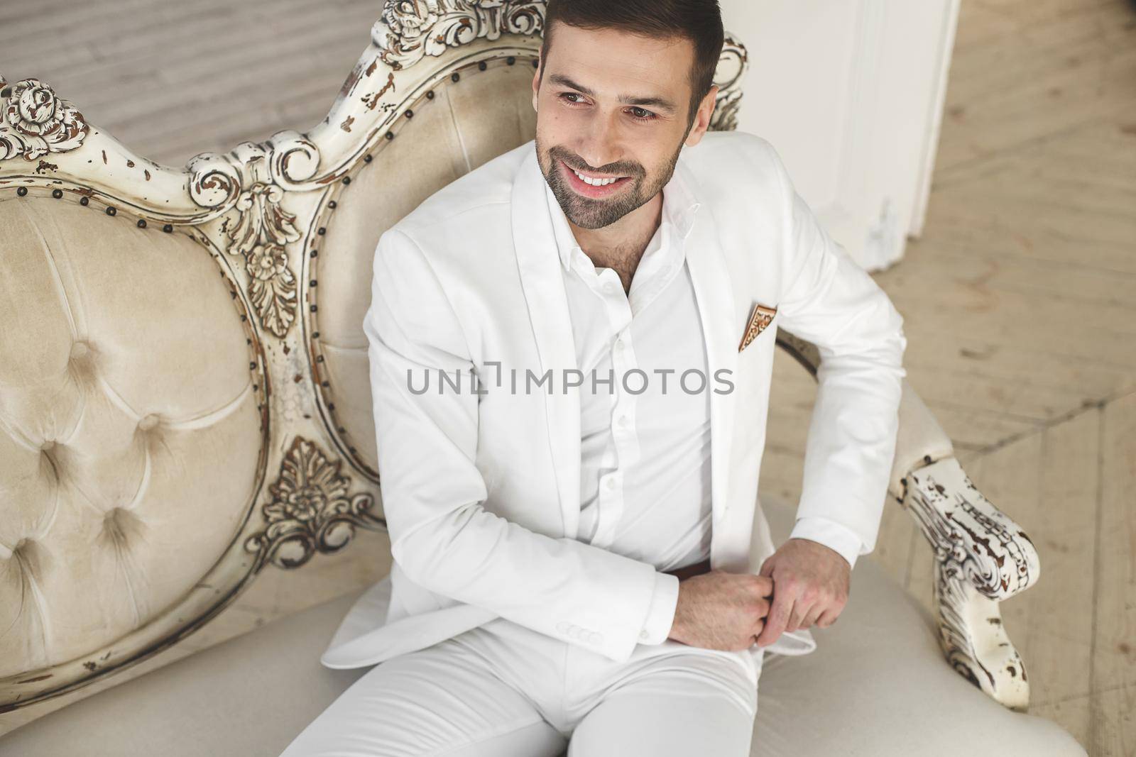 Elegant young handsome man with a beard in a white classic suit.