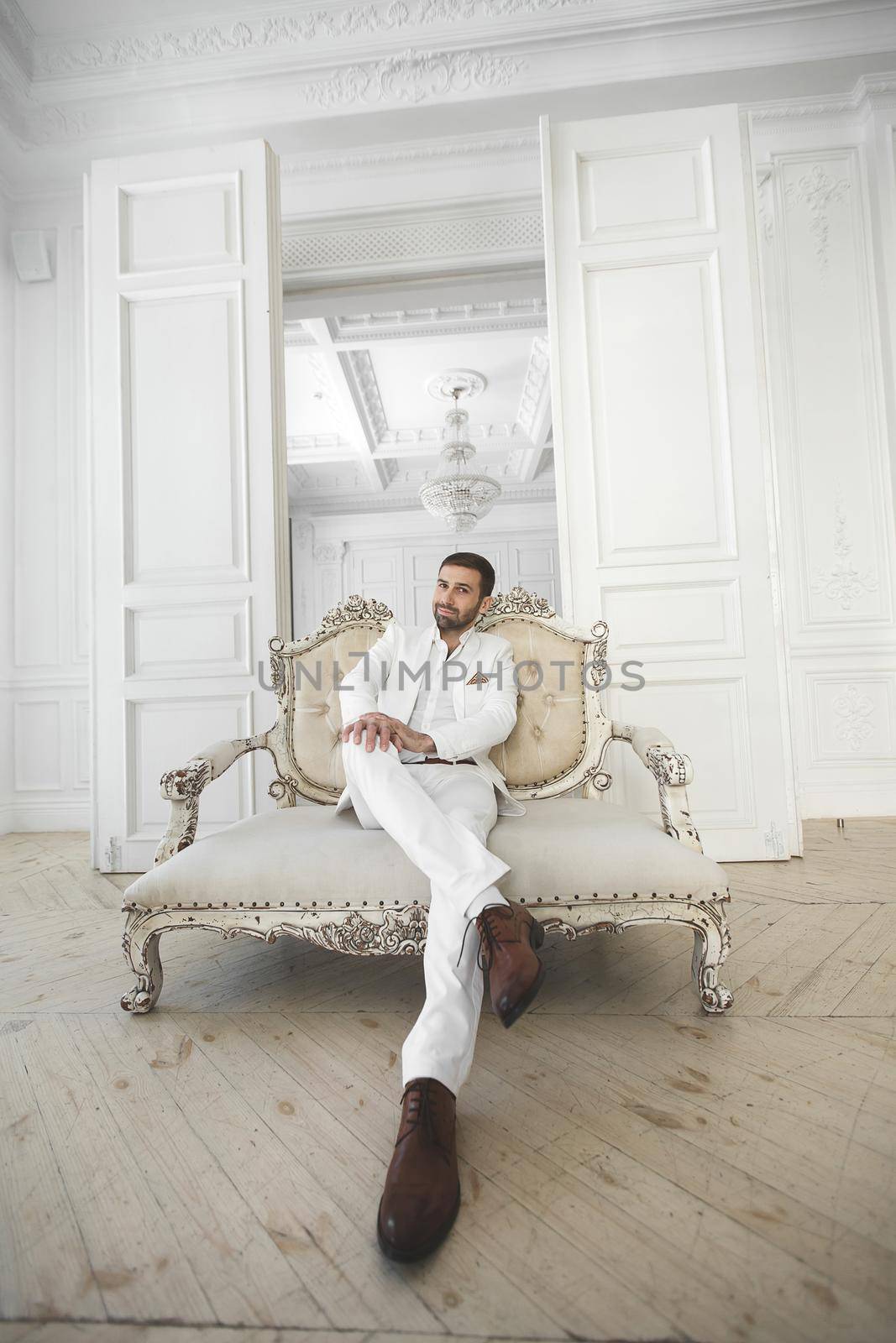 Elegant young handsome man with a beard in a white classic suit.