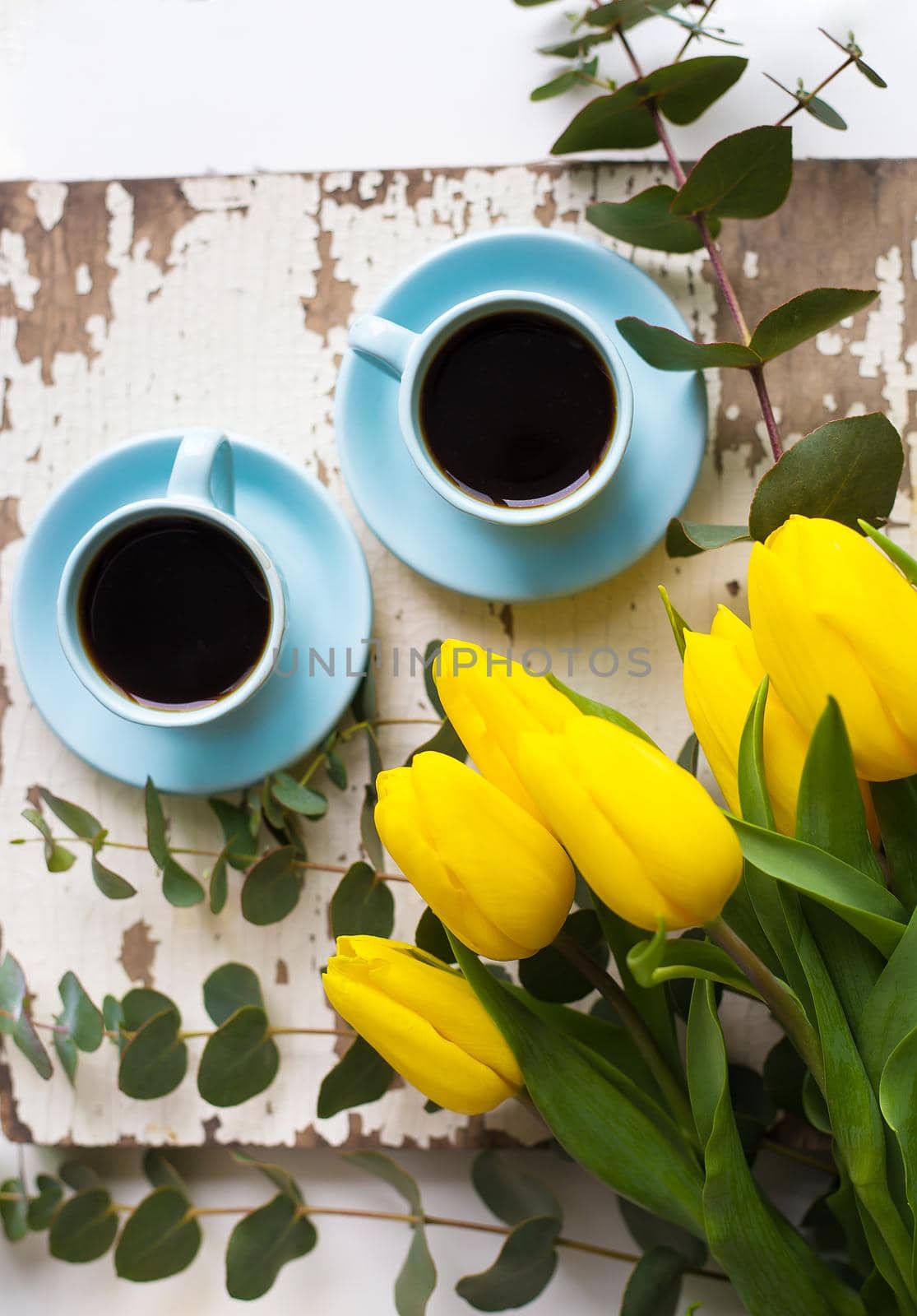 two blue cup of coffee with yellow tulips on an old table, close-up