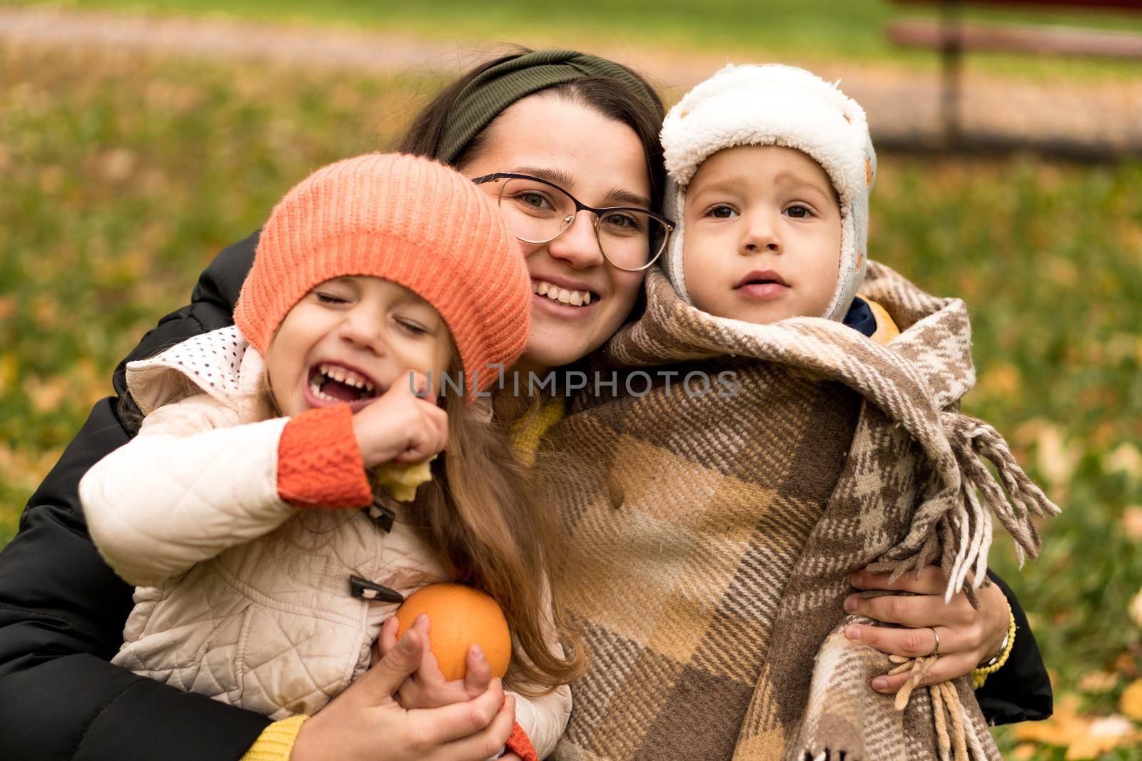 Young Woman Mom And Little Cute Preschool Minor Children In Orange Plaid At Yellow Fallen Leaves Nice Smiling Look At Camera In Cold Weather In Fall Park. Childhood, Family, Motherhood, Autumn Concept by mytrykau