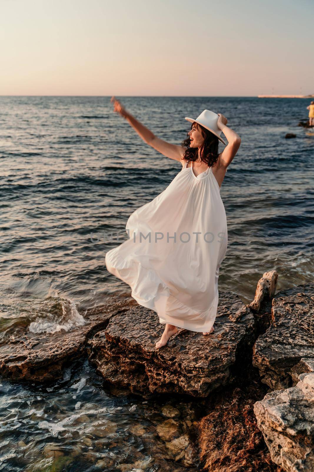 A woman in a white dress and hat is standing on the beach enjoying the sea. Happy summer holidays.