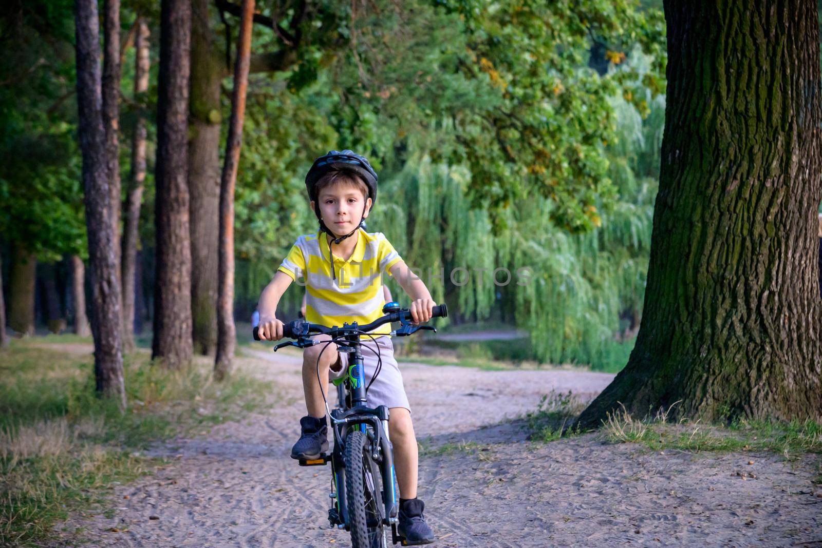 Portrait of happy toddler child boy riding on bike with helmet. He rides from a small hill, through a sandy forest path. Sport concept: kids ride bicycle first bike active toddler kid.