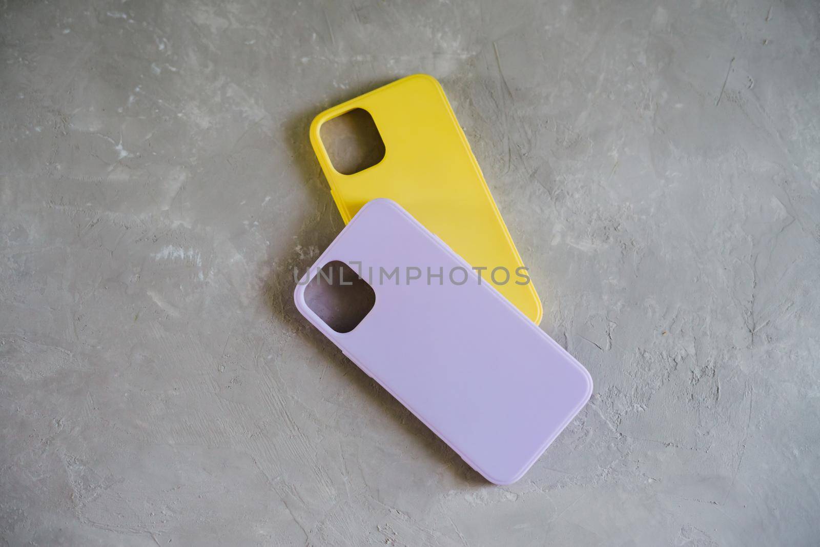 Yellow and lilac protective cases for smartphone. Two silicone cases on a textured gray background.
