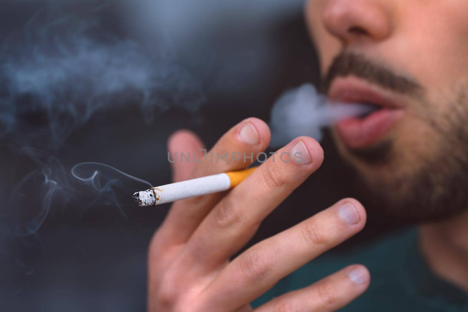 Closeup of young man smoking cigarette. Smoking addiction and bad habit concept by DariaKulkova