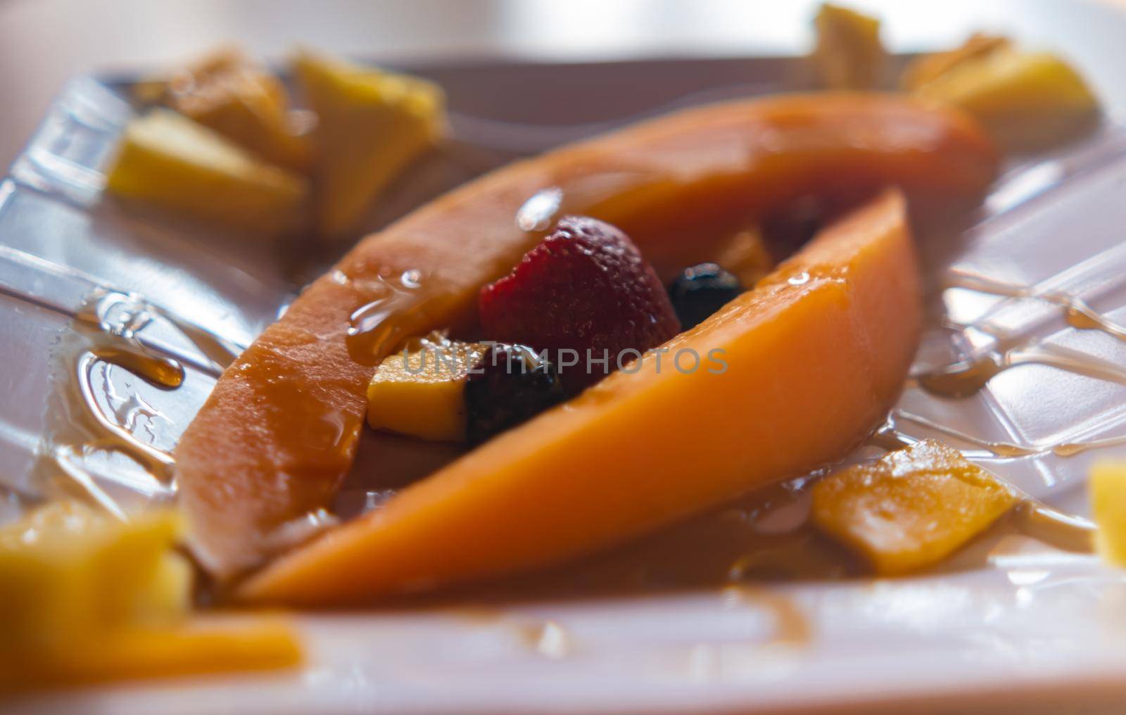 Fresh fruit slices and honey on square porcelain plate by Kanelbulle