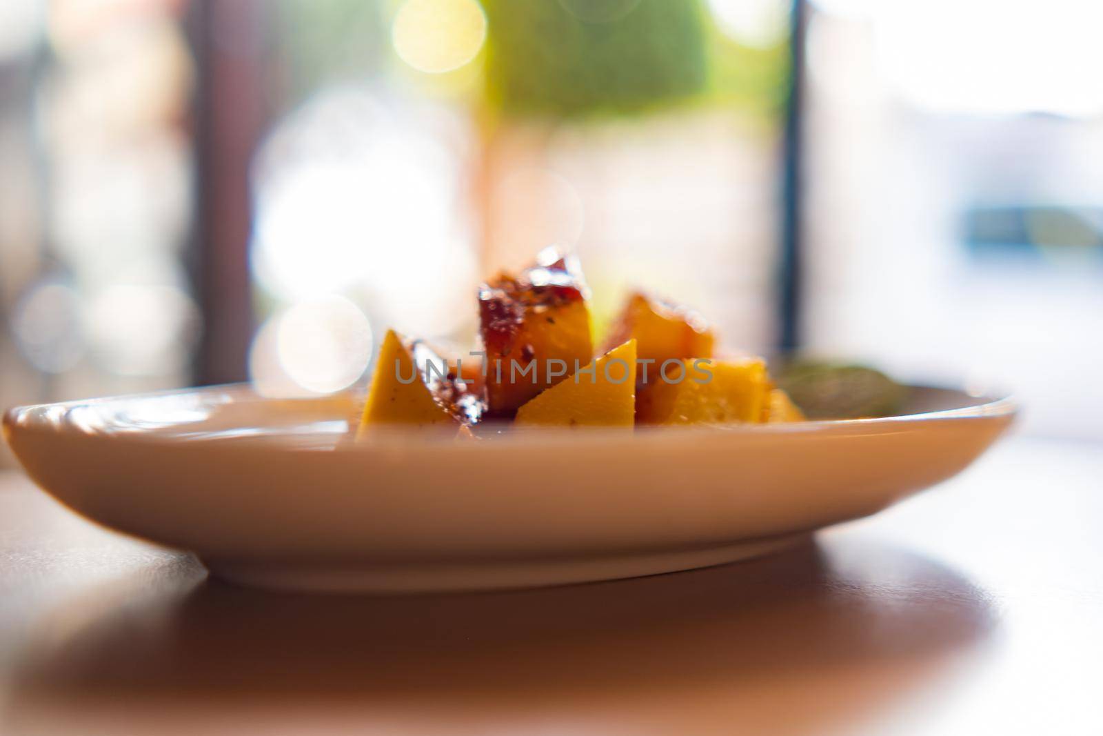 Plate of chopped mango with chili powder and Mexican chamoy sauce with blurry background. Fresh tropical fruit slices with spicy and sour condiment above wooden table. Healthy food and snacks